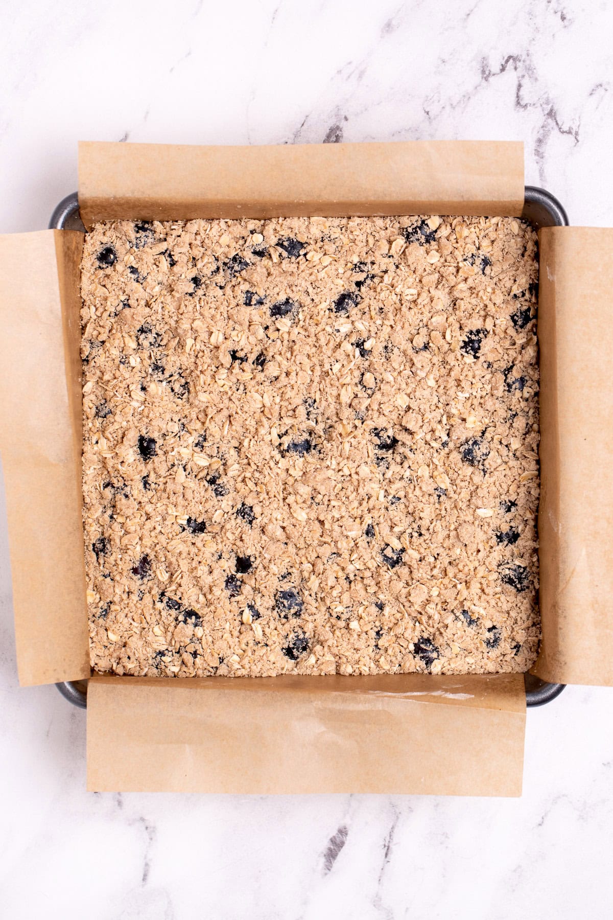 A baking pan lined with parchment paper with blueberry oatmeal bars before being baked.