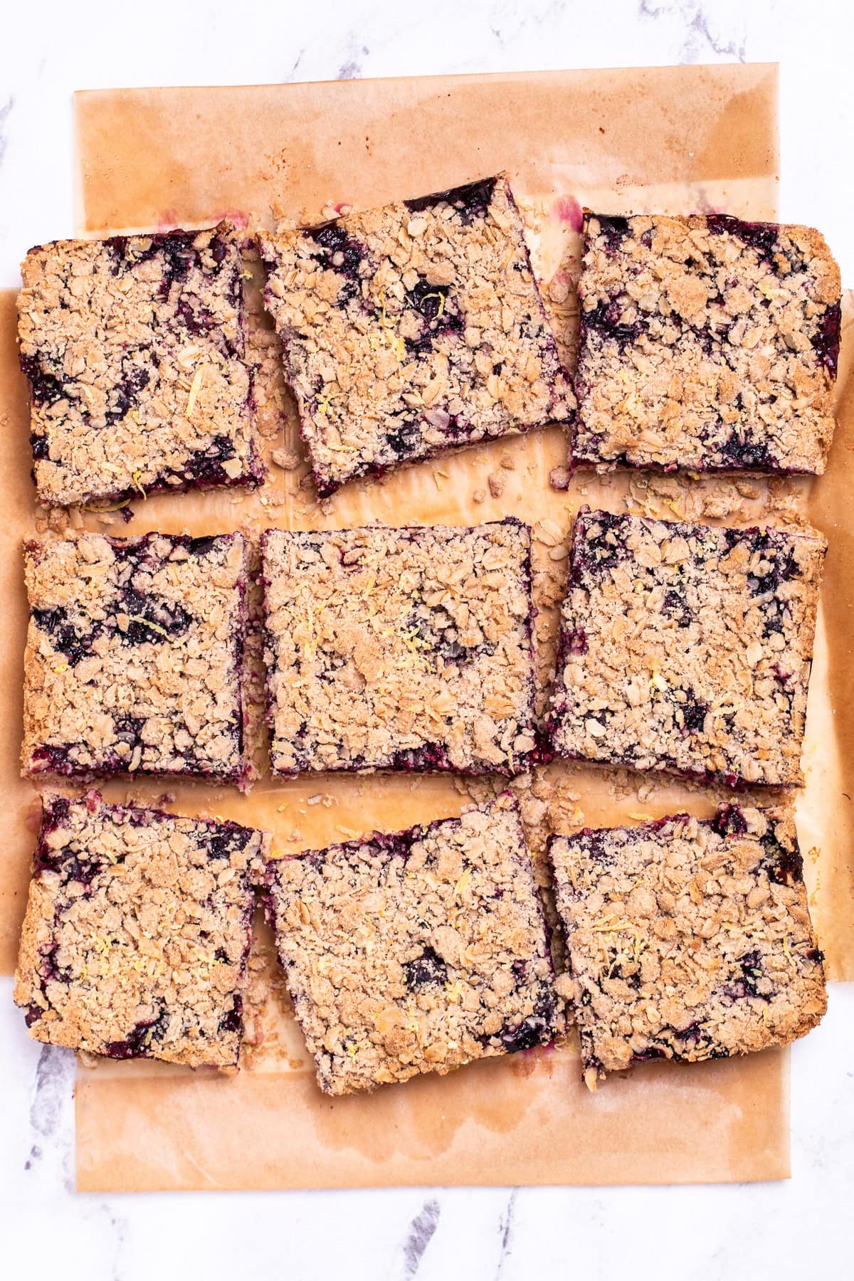 Nine blueberry oatmeal bars on parchment paper resting on a table.