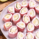 A plate resting on a cutting board with pieces of dill pickle roll ups ready to be served, with pickle spears next to it.