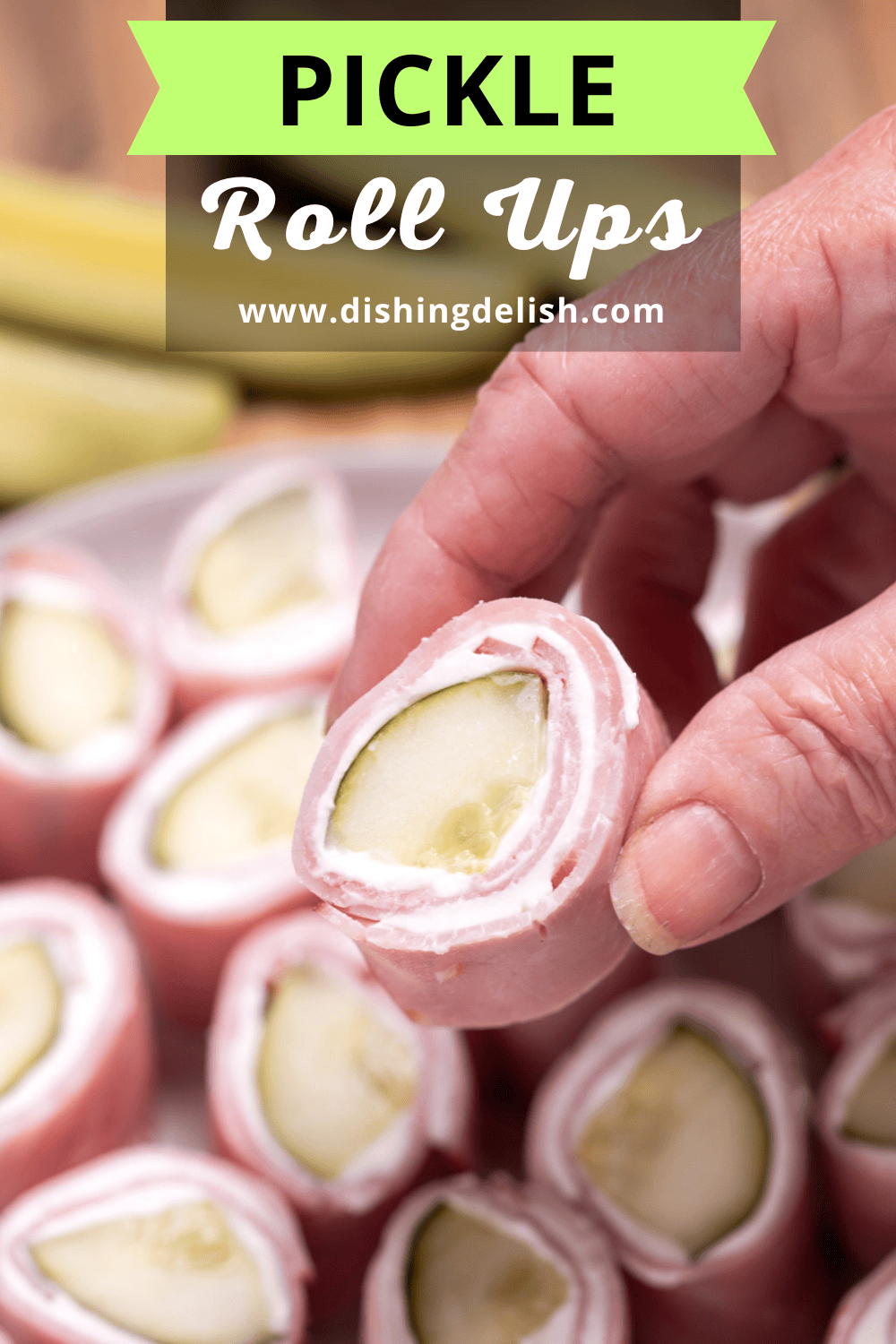Pinterest pin with a plate resting on a cutting board with pieces of dill pickle roll ups ready to be served, with pickle spears next to it. A hand is lifting one up.