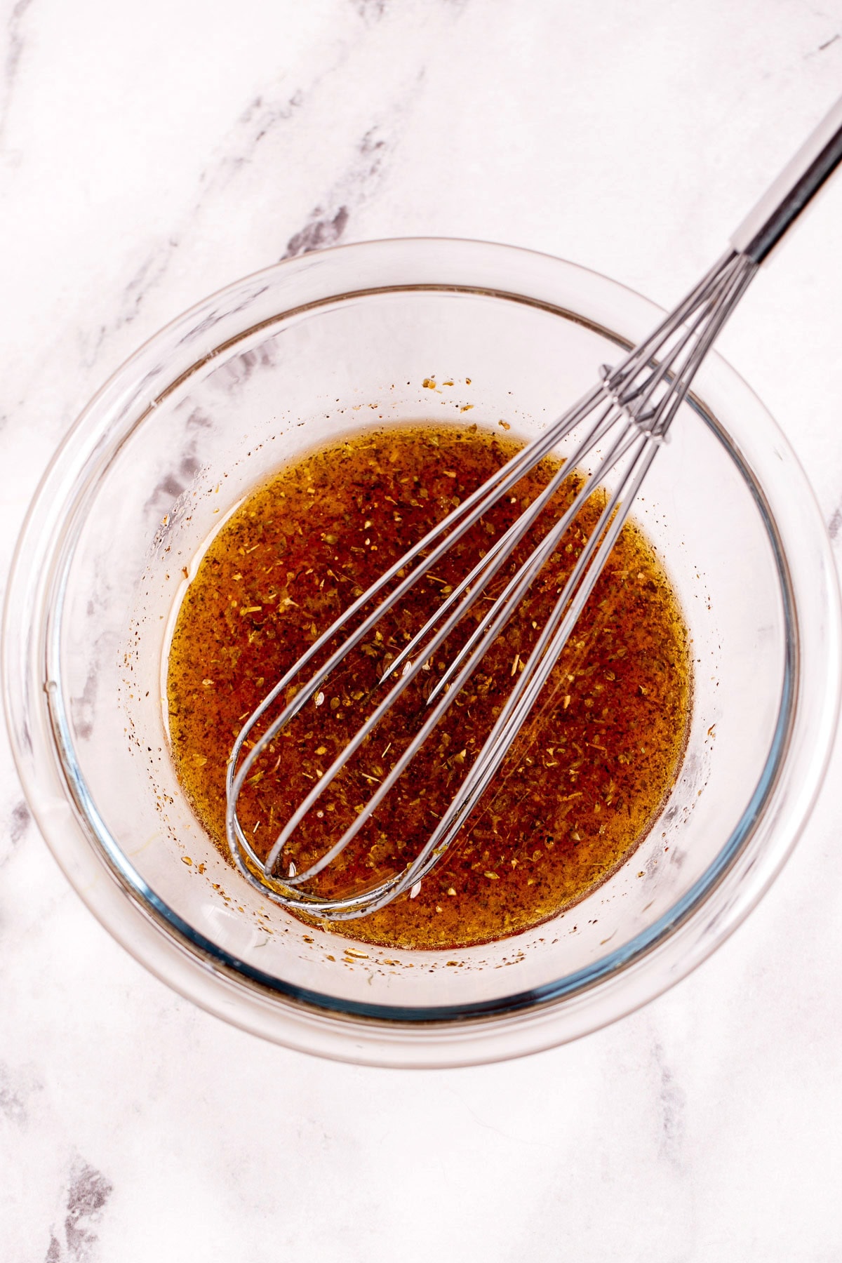 A glass bowl on a table with vinaigrette dressing and a whisk in the bowl.