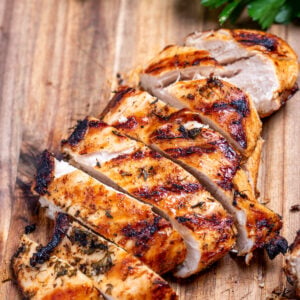 A cutting board with Greek marinated chicken sliced next to fresh parsley.