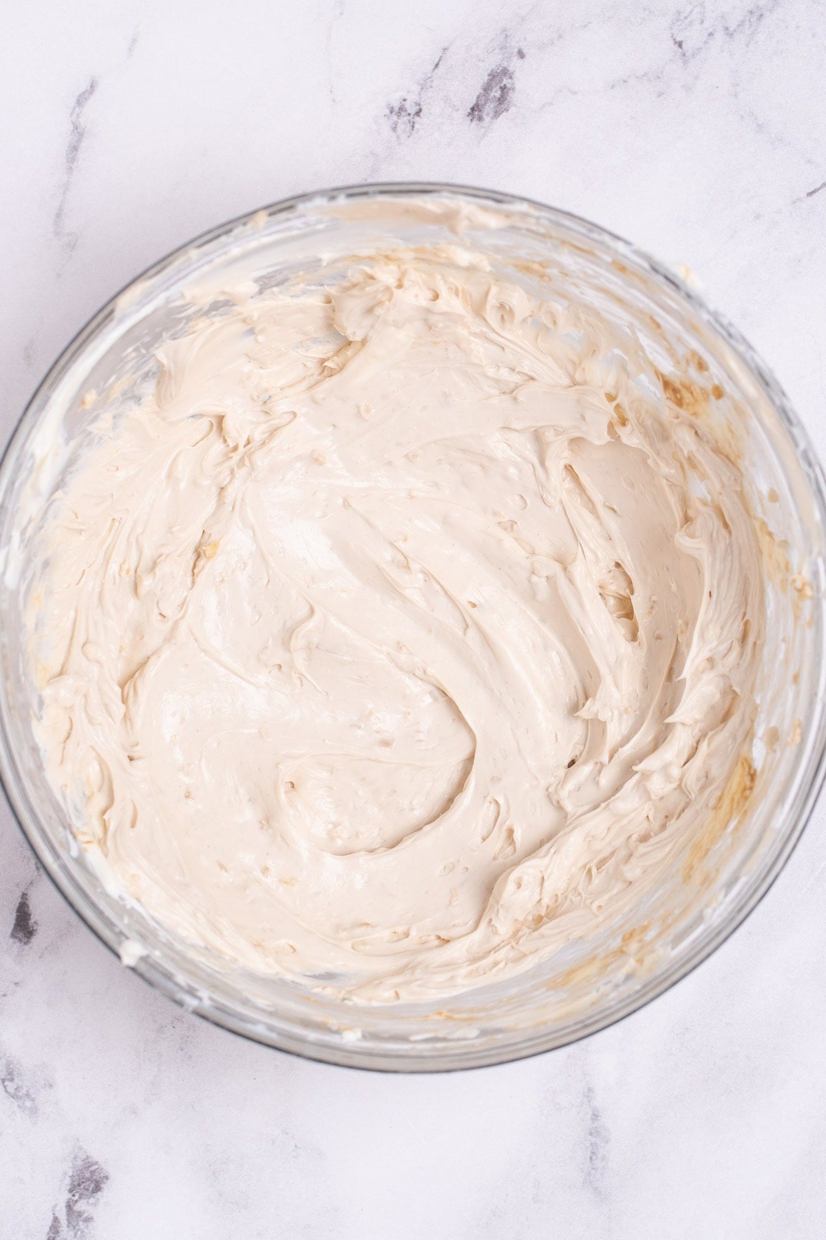 A glass bowl of whipped cream cheese with spices and sour cream on a table.