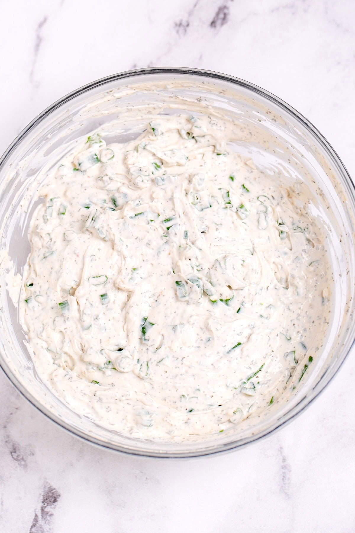 A glass bowl of green onion dip just after being mixed together on a table.