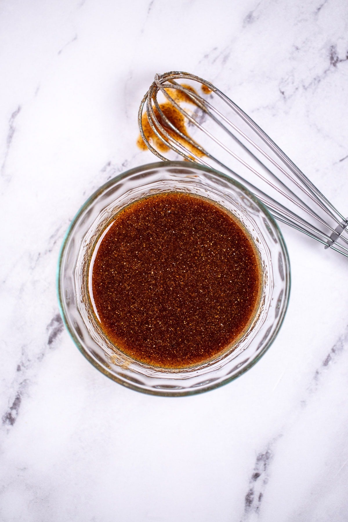 A small bowl of chicken marinade next to a whisk on a table.