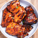 A bowl of BBQ chicken thighs, sitting on a cutting board.