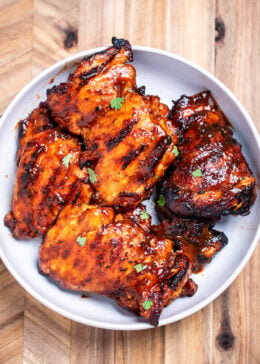 A bowl of BBQ chicken thighs, sitting on a cutting board.