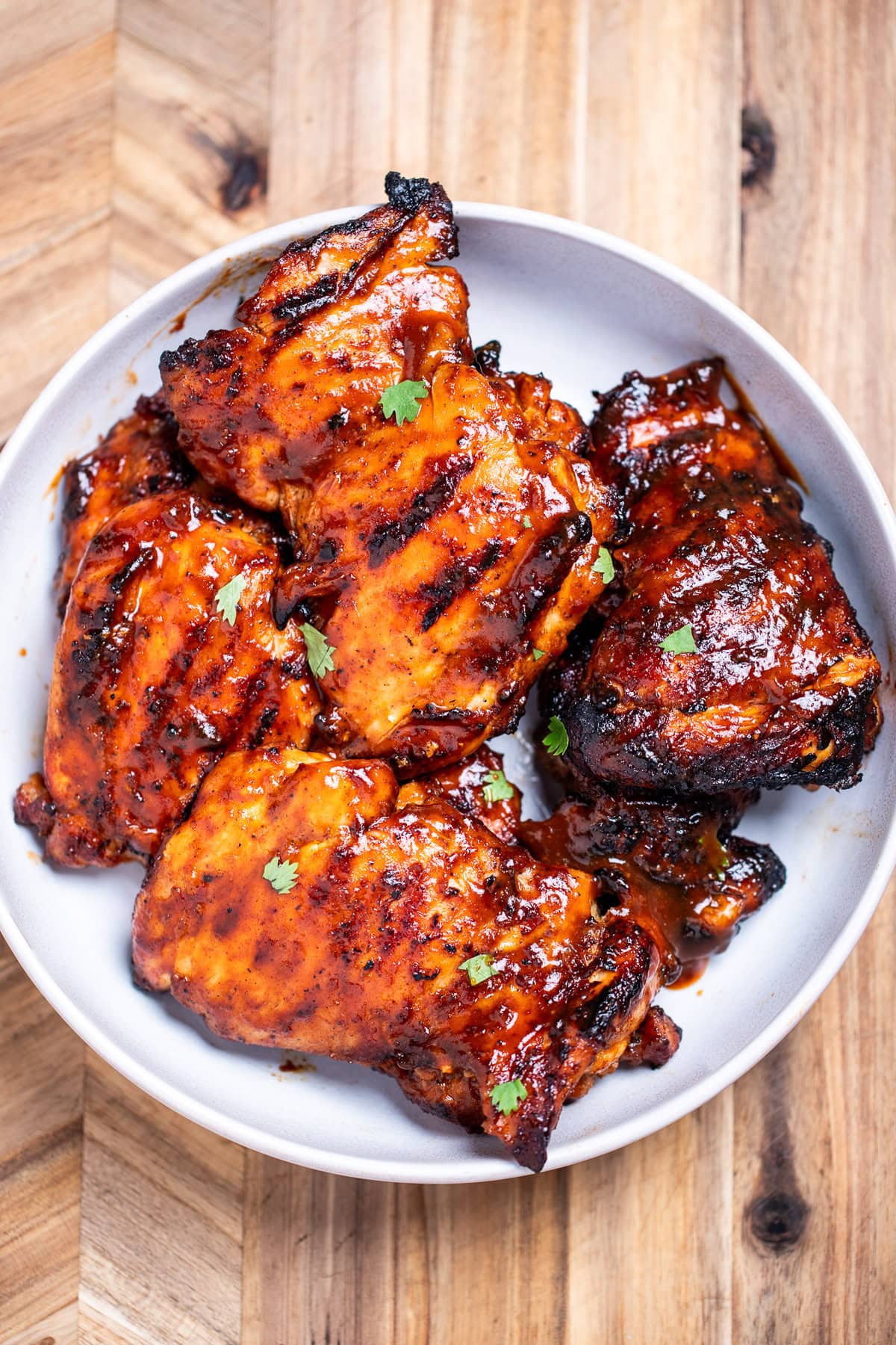 A bowl of BBQ chicken thighs, sitting on a cutting board.