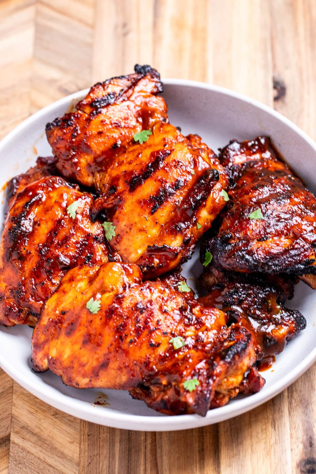 A bowl of BBQ chicken thighs, sitting on a cutting board.