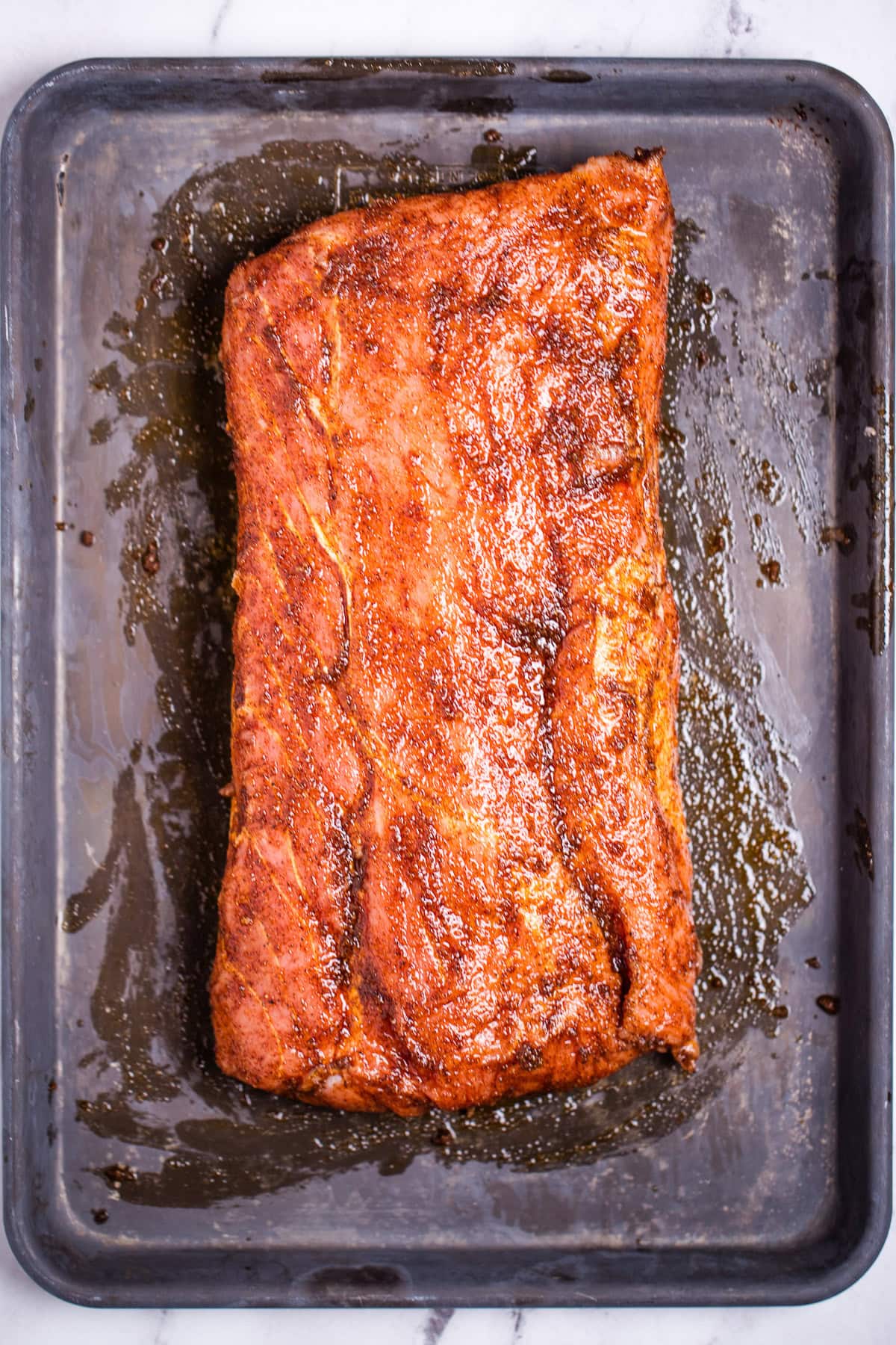 A sheet pan with a raw pork loin roast covered in olive oil and seasoning rub.