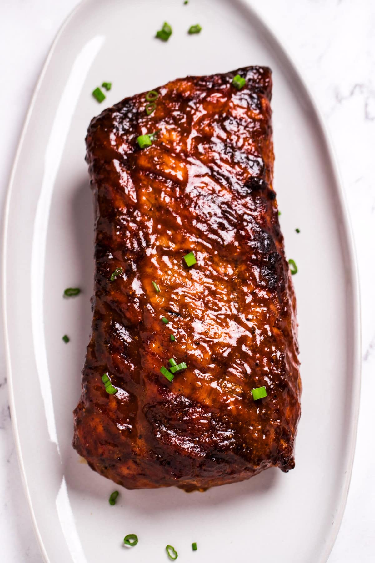 A plate with a grilled bbq pork loin roast smothered in bbq sauce and topped with green onions.