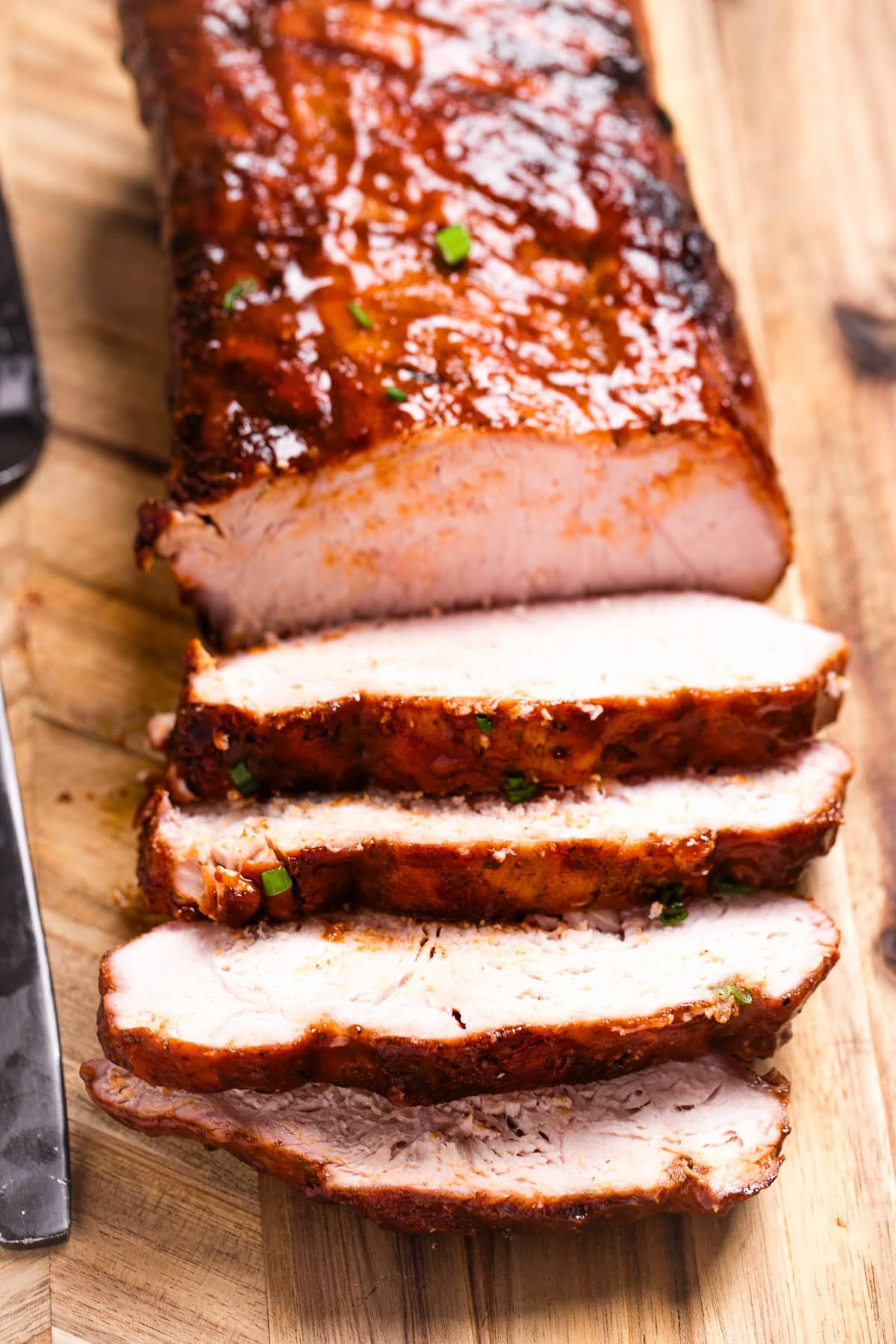 A cutting board with a BBQ pork loin and a few slices in the front.