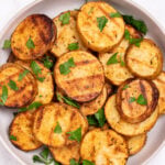 A serving bowl with grilled potato slices topped with chopped fresh parsley. The potato slices have nice grill marks.