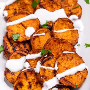 A plate of grilled sweet potatoes topped with drizzled sour cream and chopped fresh parsley.