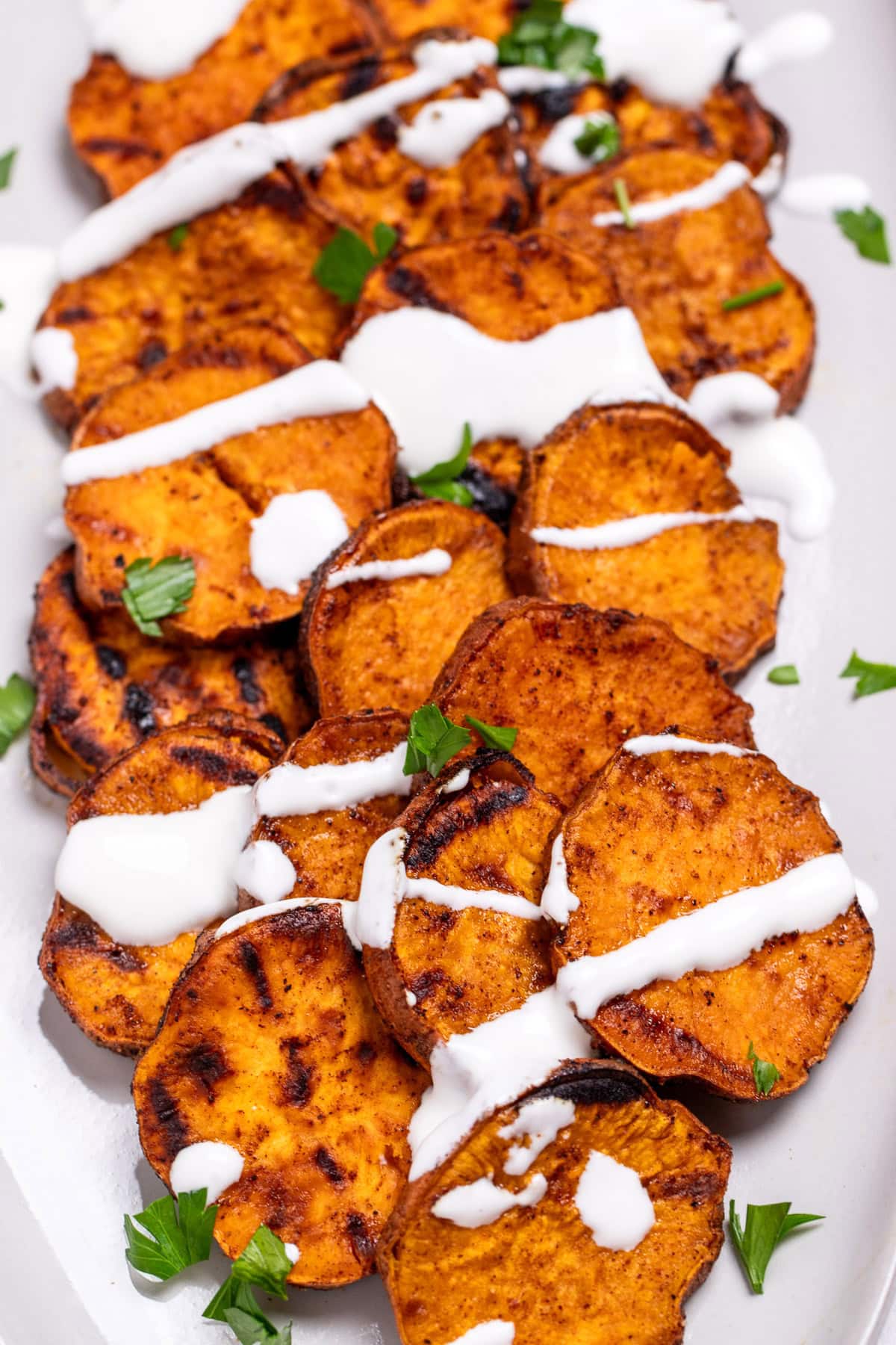 A plate of grilled sweet potatoes topped with drizzled sour cream and chopped fresh parsley.