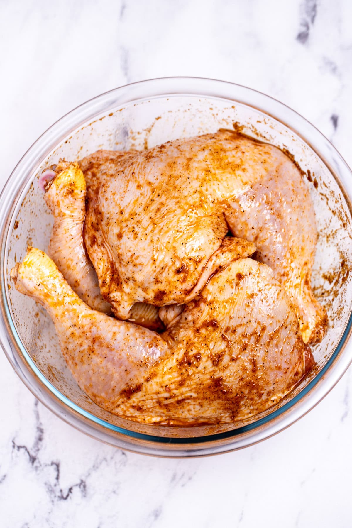 A mixing bowl with chicken quarters covered in olive oil and seasoning.