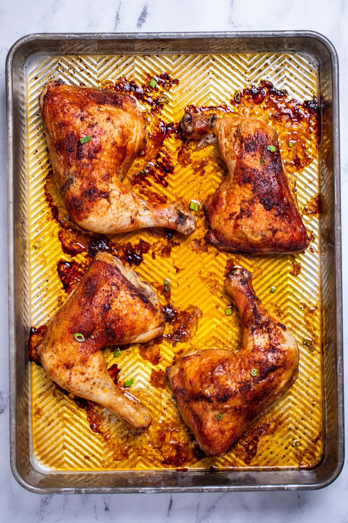 A roasting pan with four chicken leg quarters after being roasted in the oven.