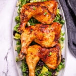 Three chicken quarters on a serving dish on top of salad greens.