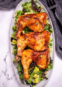 Three chicken quarters on a serving dish on top of salad greens.