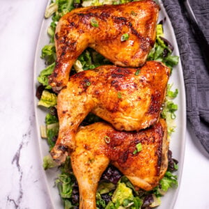 Three chicken quarters on a serving dish on top of salad greens.