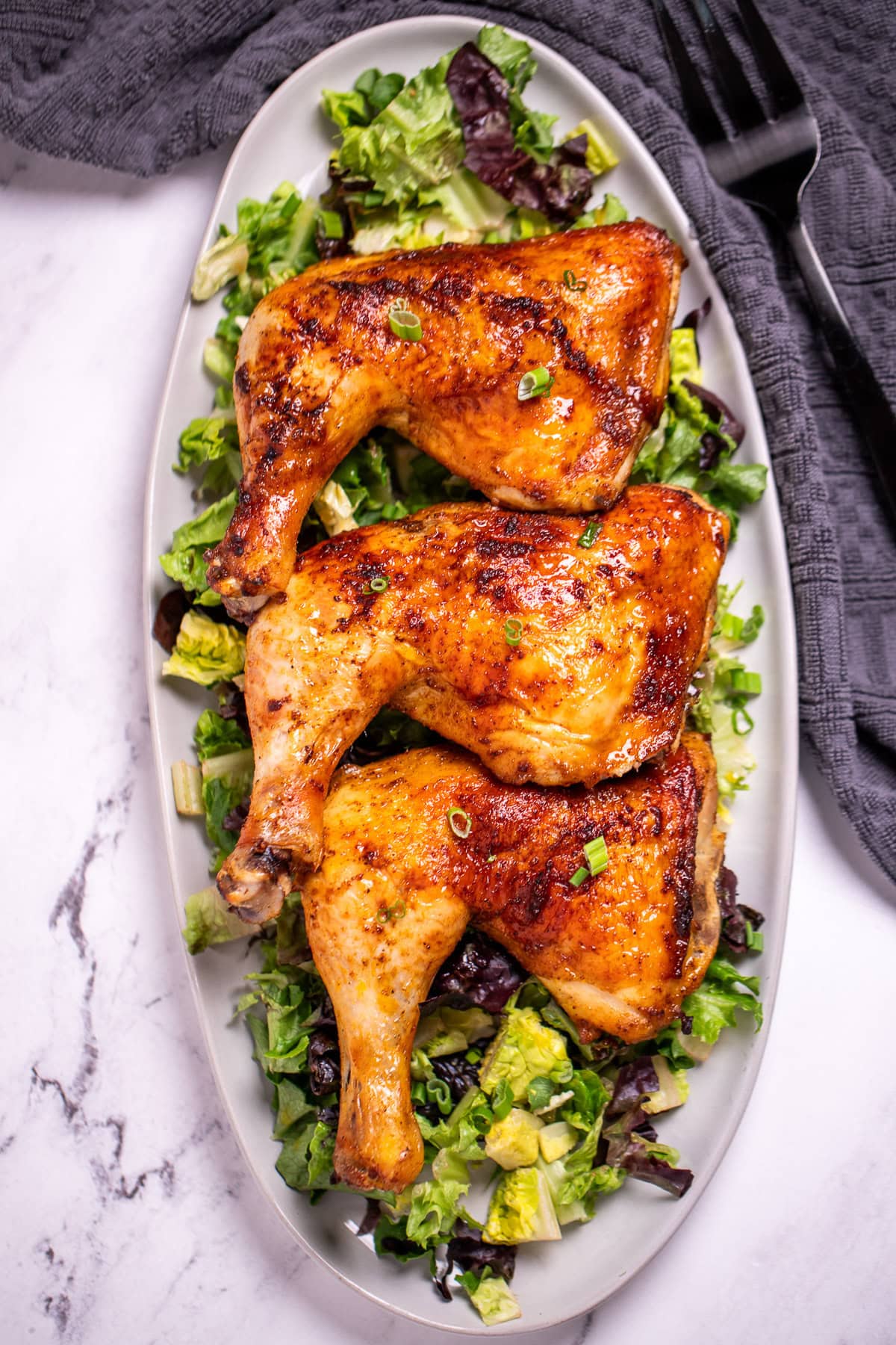 Three chicken quarters on a serving dish on top of salad greens.