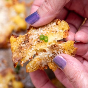 Two hands holding a garlic parmesan smashed potato while breaking it in half.