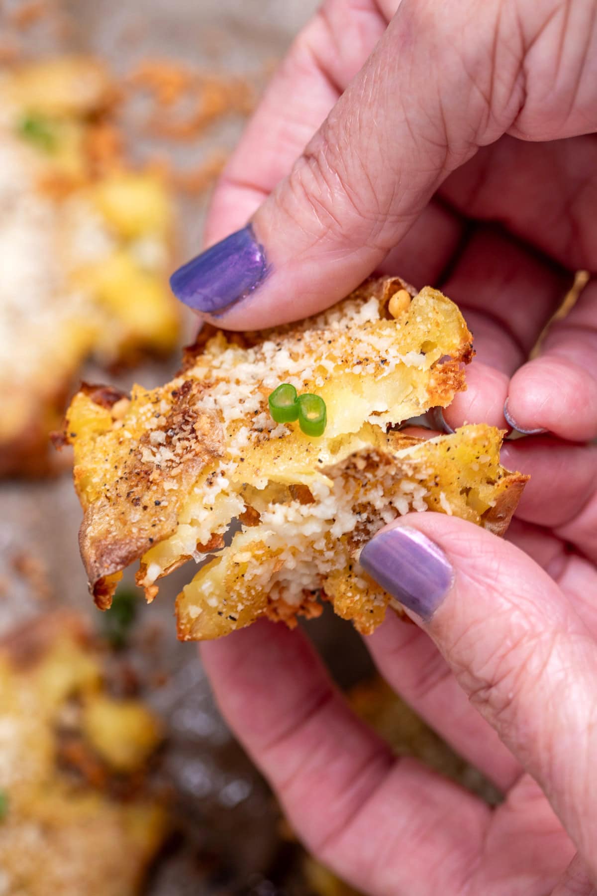 Two hands holding a garlic parmesan smashed potato while breaking it in half.
