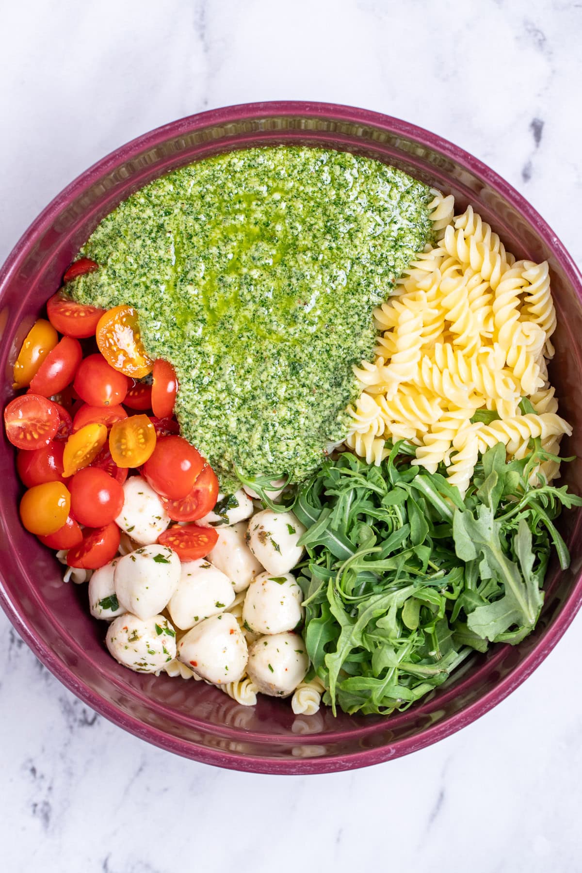 A bowl with individual ingredients for pesto pasta salad before being mixed together.