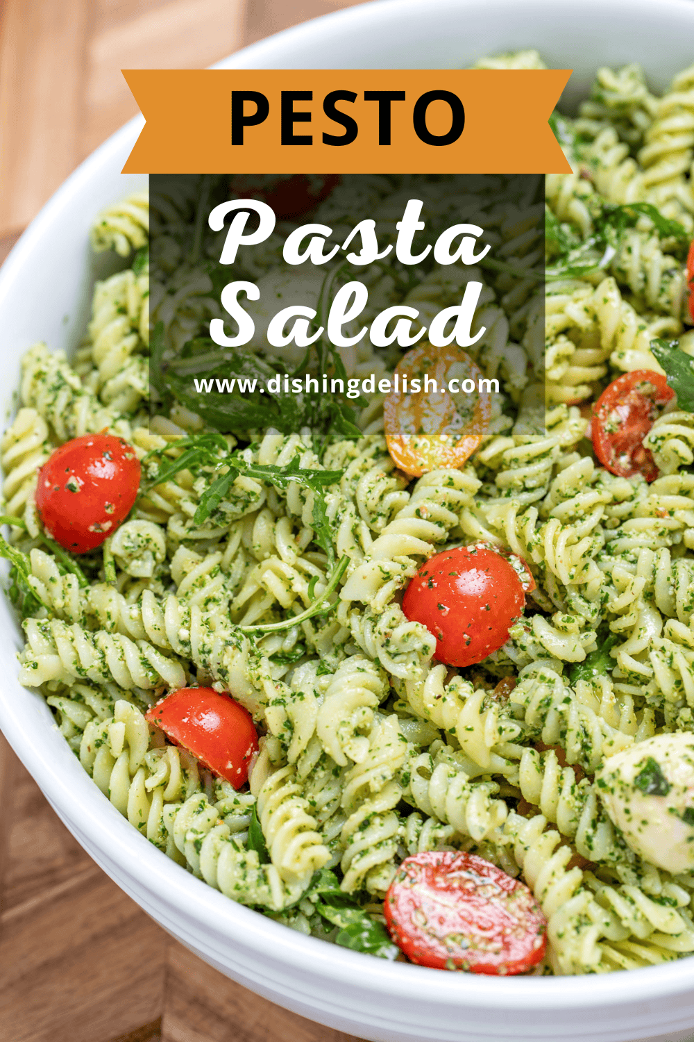 Pinterest pin with pesto pasta salad with mozzarella and cherry tomatoes in a serving bowl resting on a cutting board.