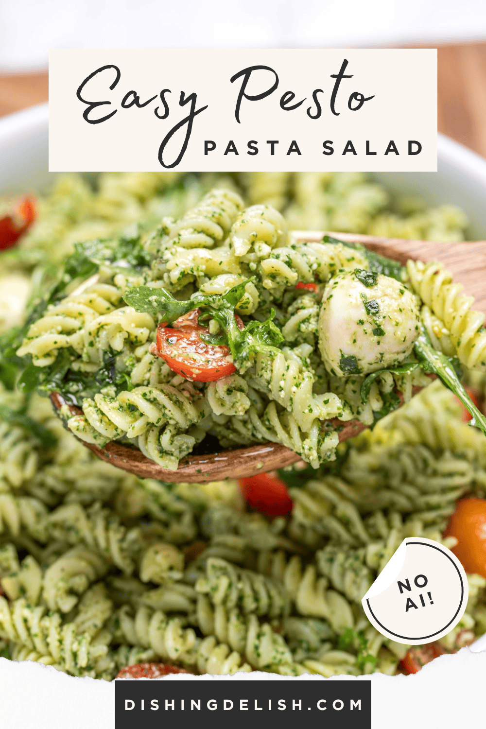 Pinterest pin with pesto pasta salad with mozzarella and cherry tomatoes in a serving bowl resting on a cutting board, with a spoon lifting some up.
