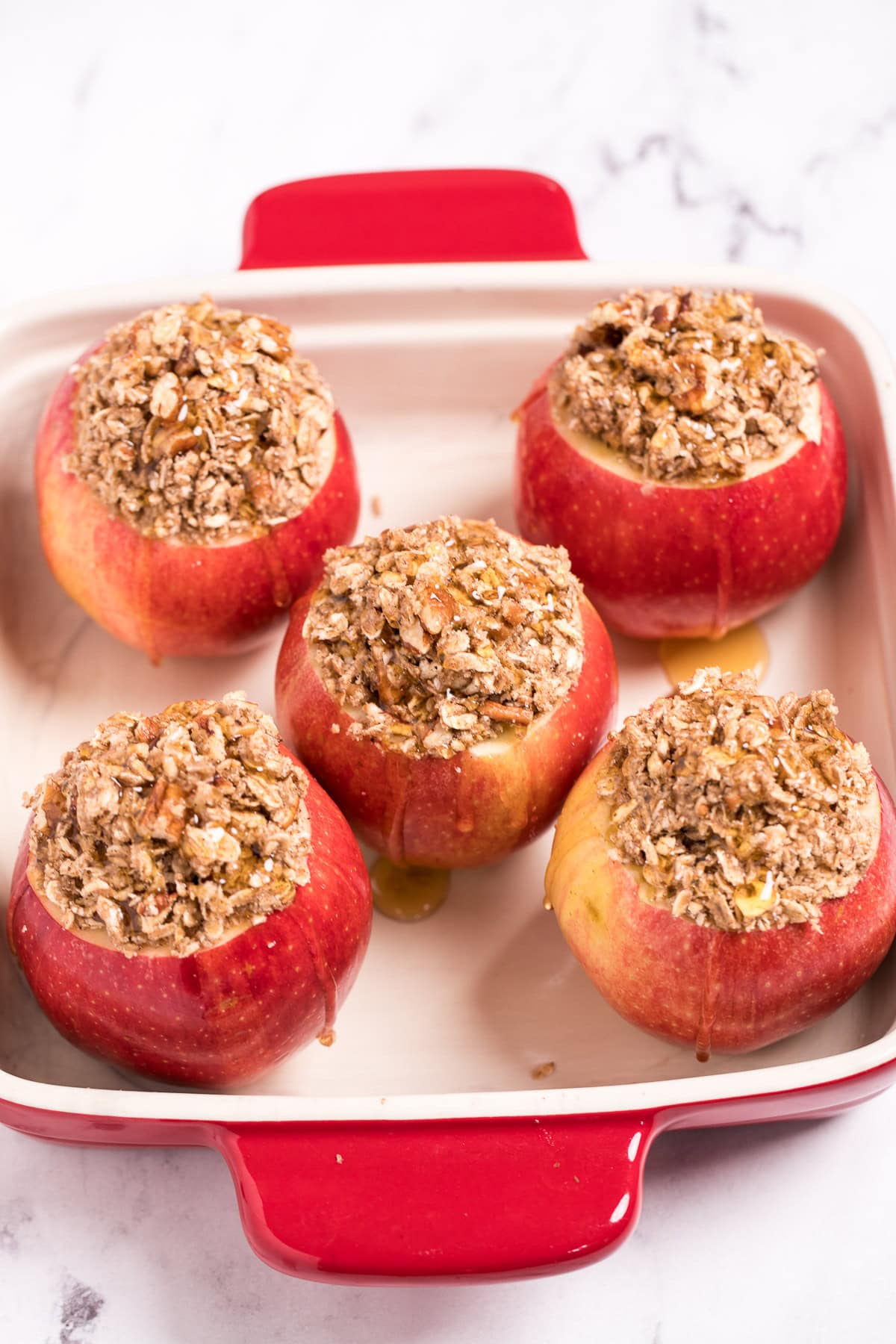 Five apples in a baking dish filled with a cinnamon oat filling, drizzled with honey.