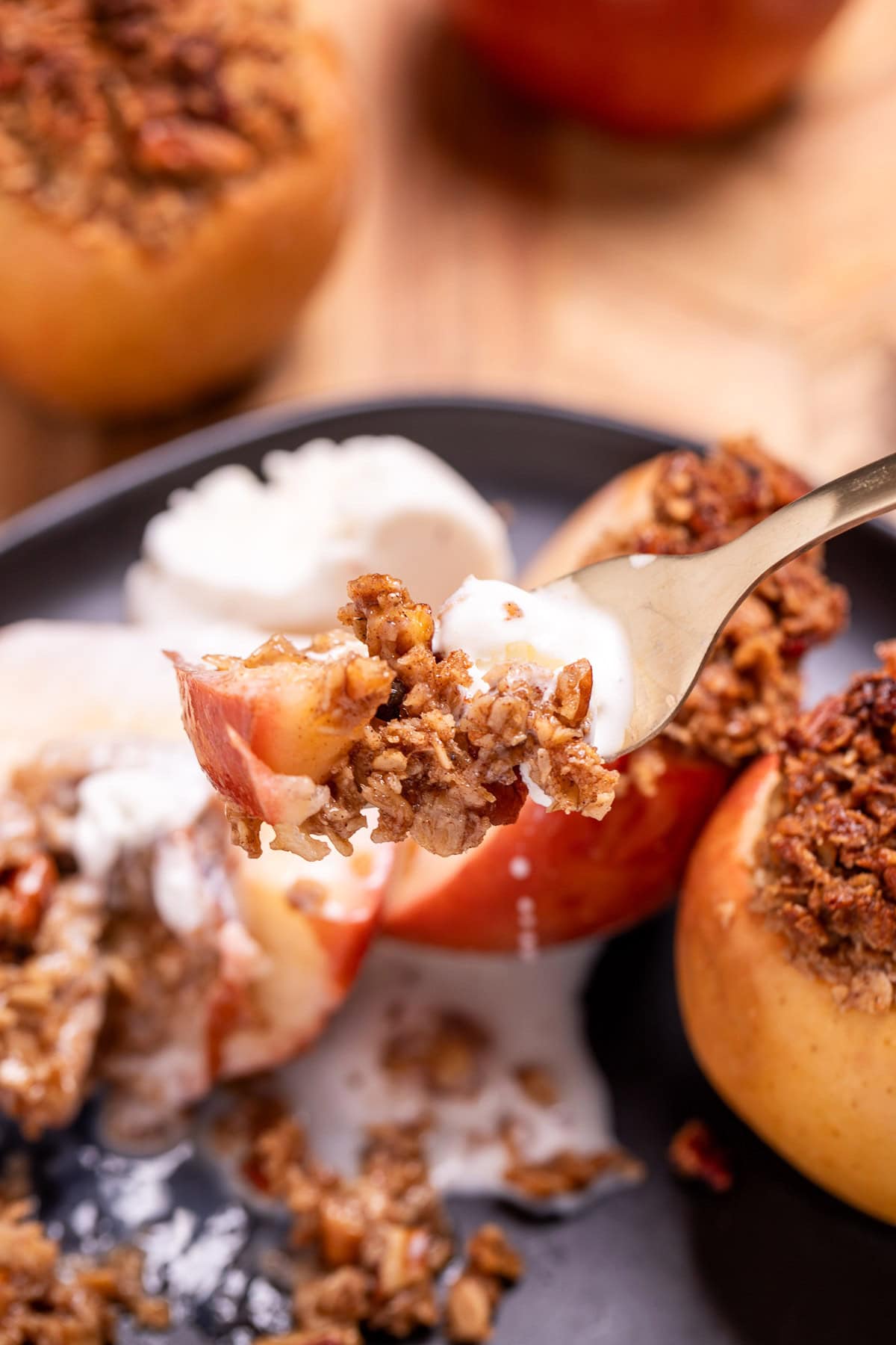 A plate with a baked apple with oat stuffing cut in half and topped with a scoop of vanilla ice cream, with a fork lifting some up.
