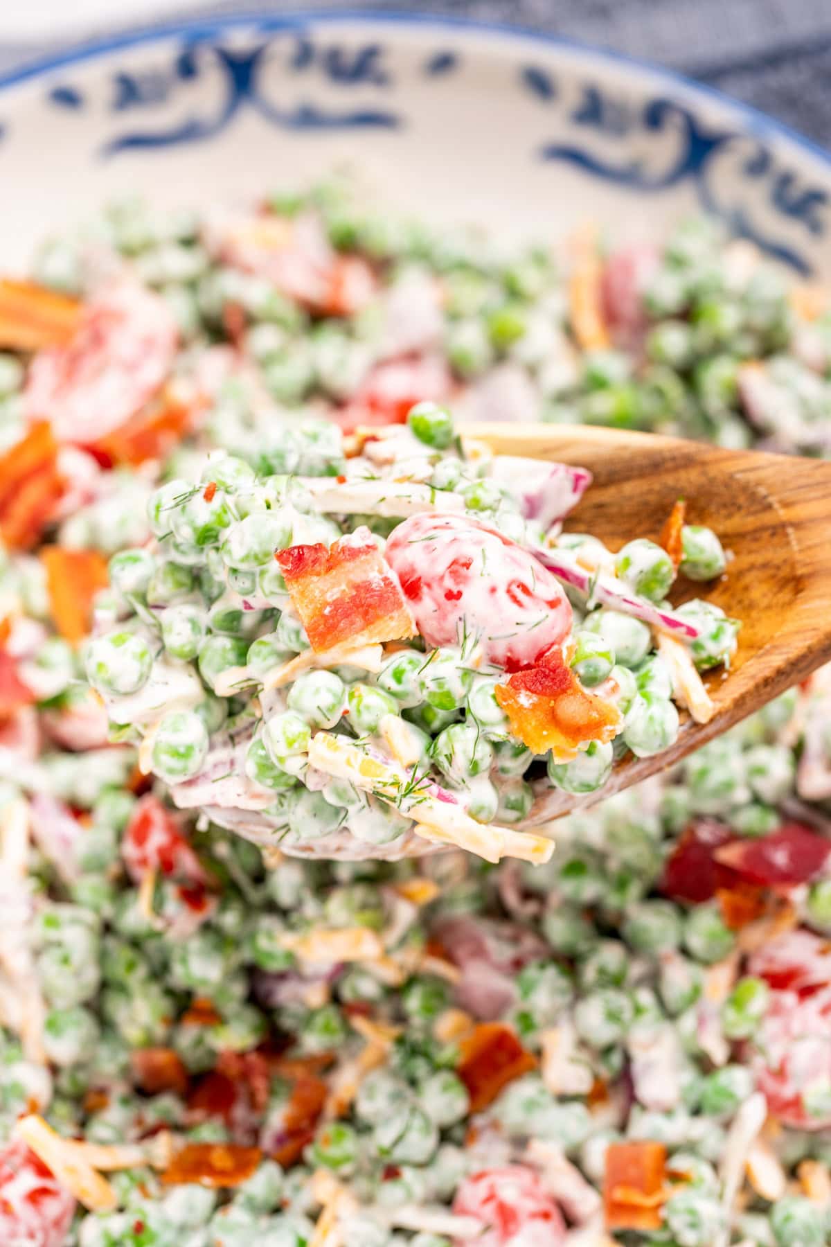 Green pea salad with a wooden spoon lifting some up, topped with crispy bacon.