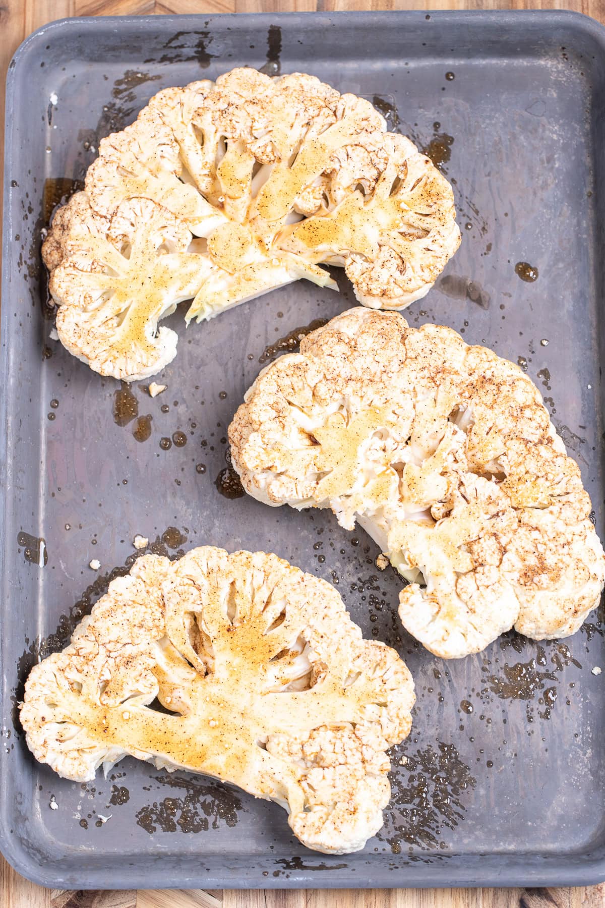 Cauliflower steaks with seasoning on a sheet pan before being grilled.