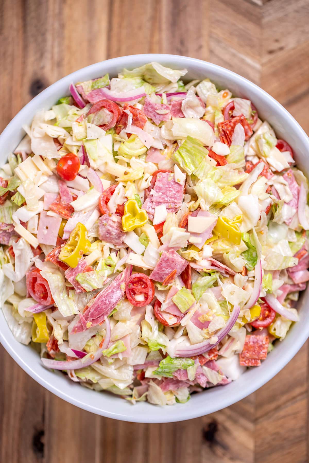 An Italian Grinder Salad (Italian Sub Salad) in a bowl on a wooden cutting board.
