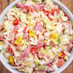 An Italian Grinder Salad (Italian Sub Salad) in a bowl on a wooden cutting board.