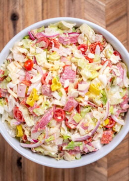 An Italian Grinder Salad (Italian Sub Salad) in a bowl on a wooden cutting board.