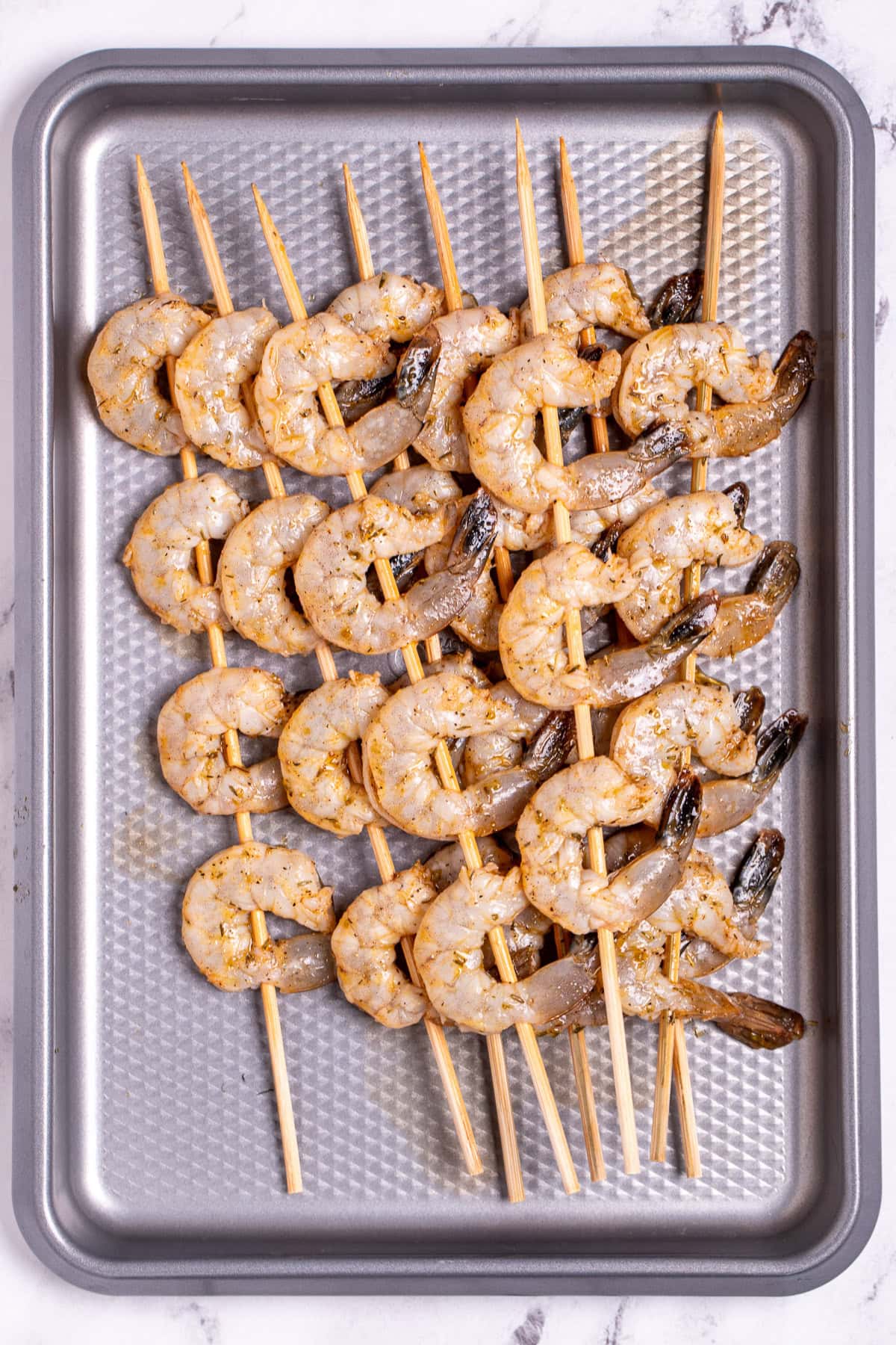 A small sheet pan with skewers of raw shrimp before being cooked.