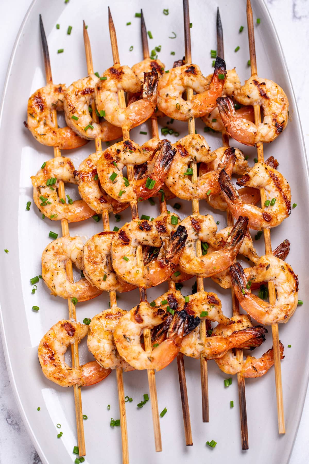 A plate on a table with grilled shrimp skewers topped with green onion.