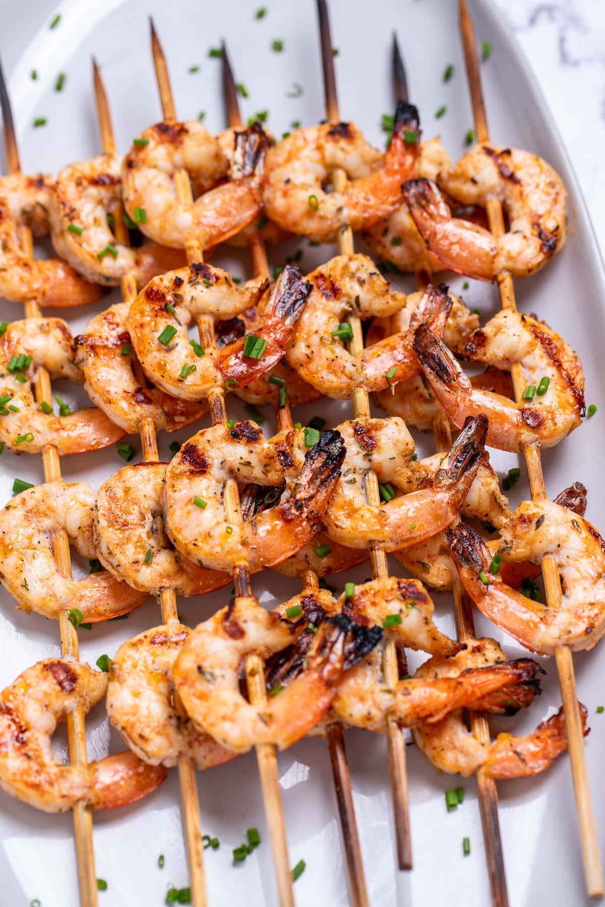 A plate on a table with grilled shrimp skewers topped with green onion.