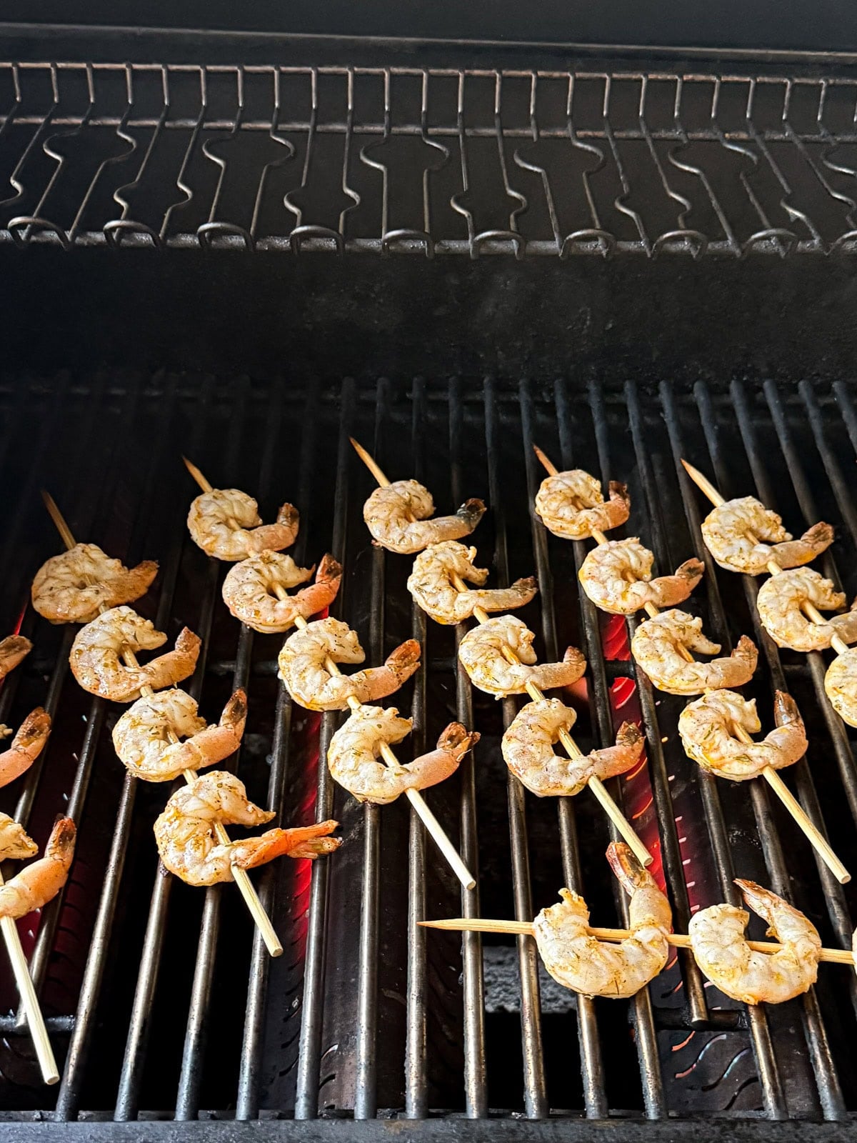 A gas grill with shrimp skewers cooking on it.