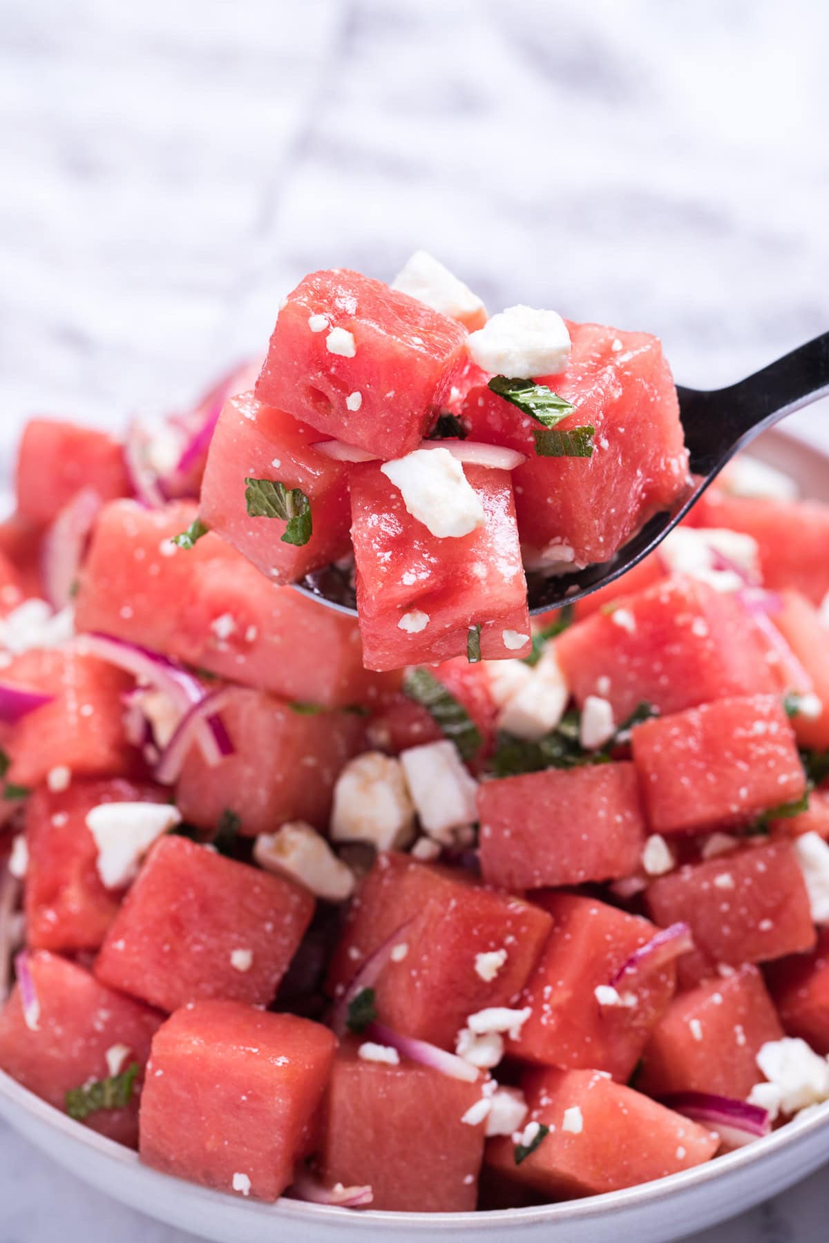 Watermelon feta salad in a bowl with a serving spoon lifting some up.