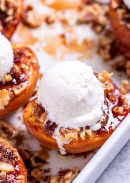 Baked peaches topped with brown sugar and pecans in a baking dish, topped with vanilla ice cream.