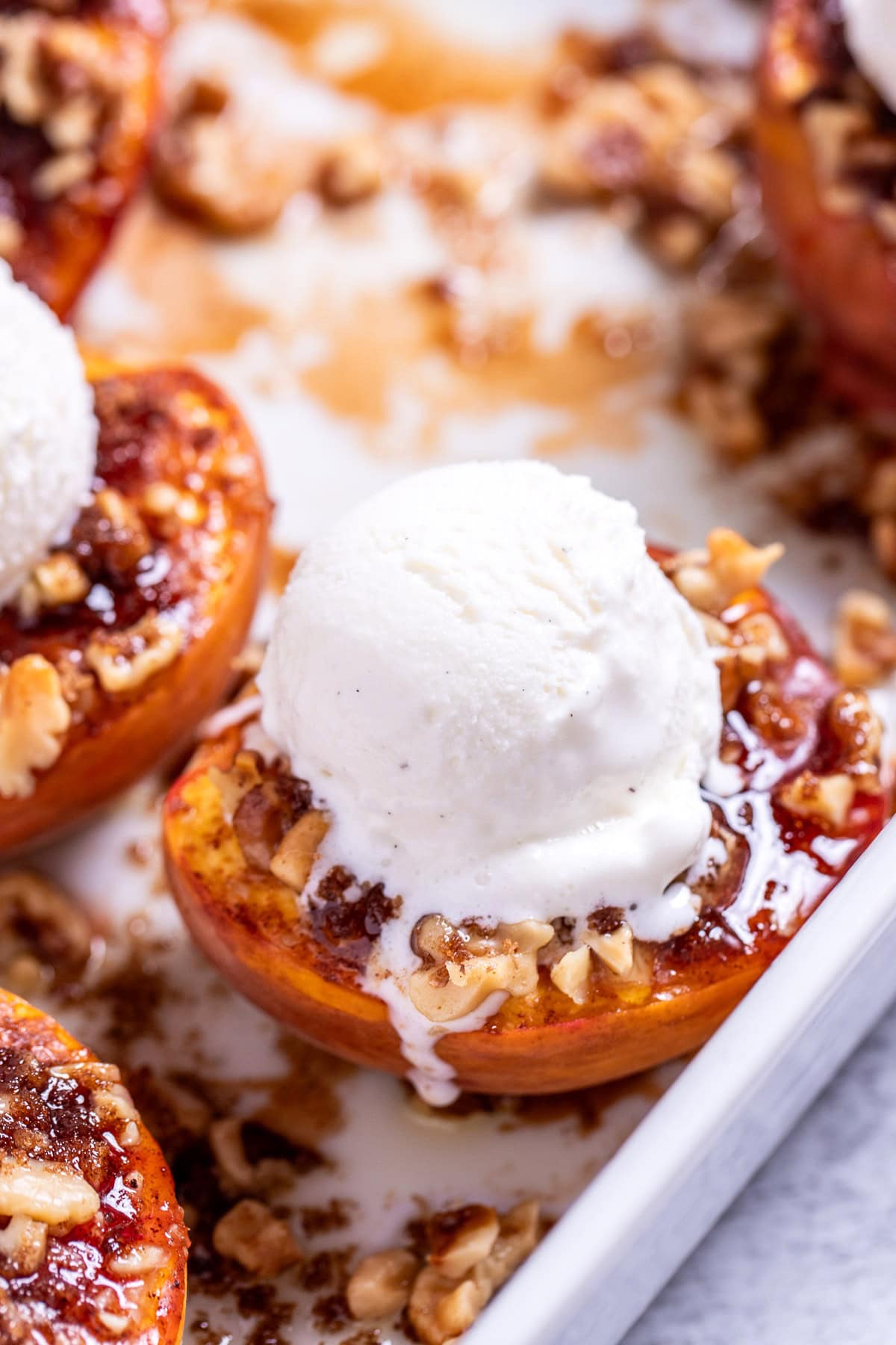 Baked peaches topped with brown sugar and pecans in a baking dish, topped with vanilla ice cream.