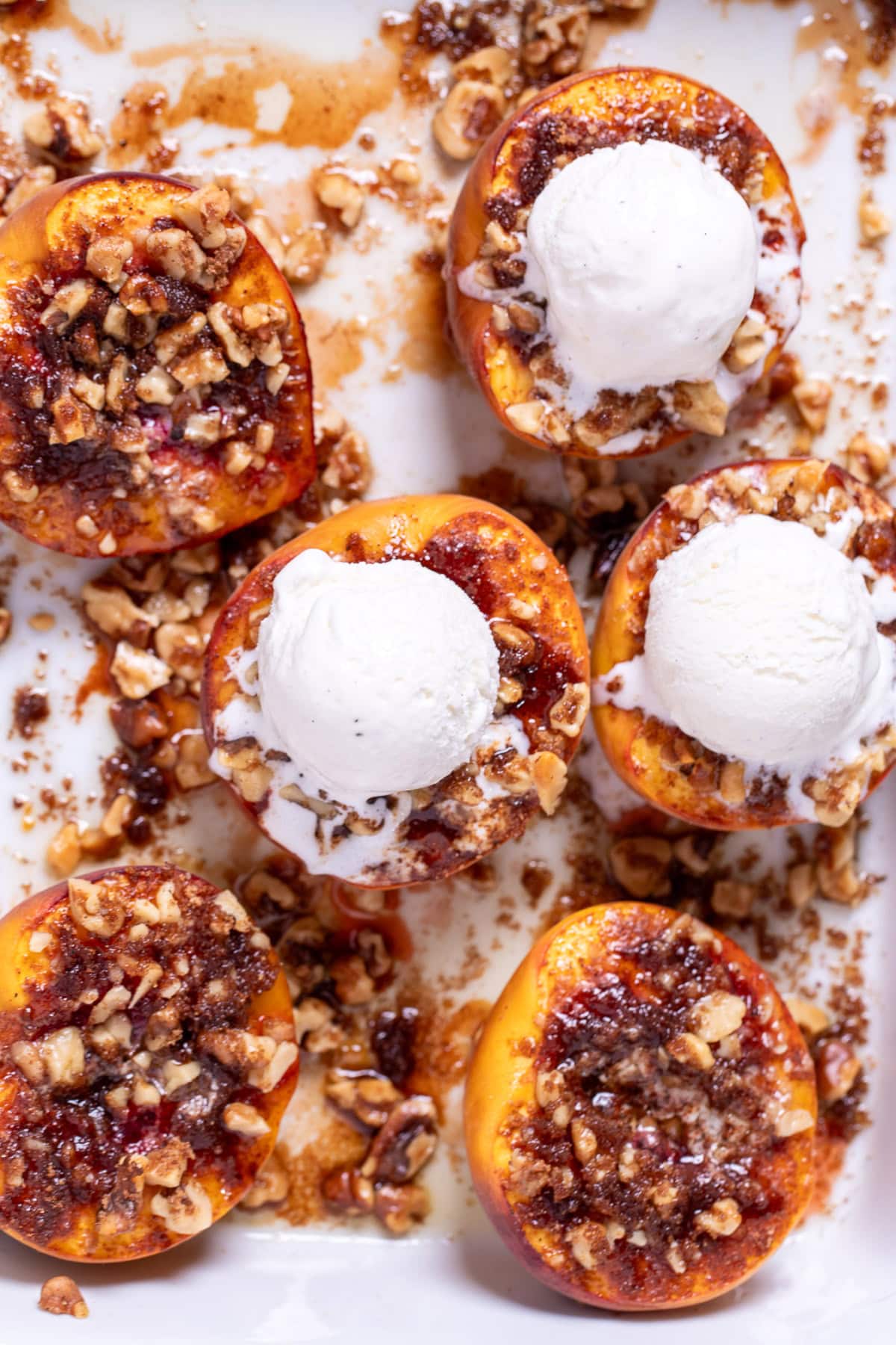 Baked peaches topped with brown sugar and pecans in a baking dish, topped with vanilla ice cream.