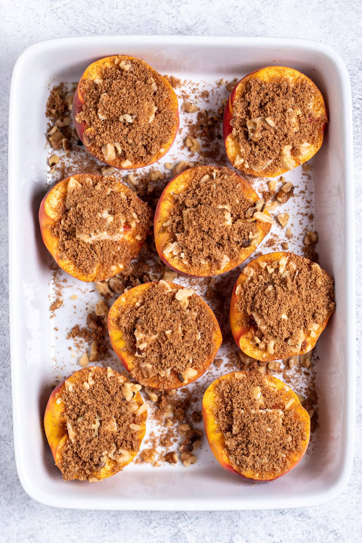 Peach halves open-side-up with a brown sugar topping in a baking dish.
