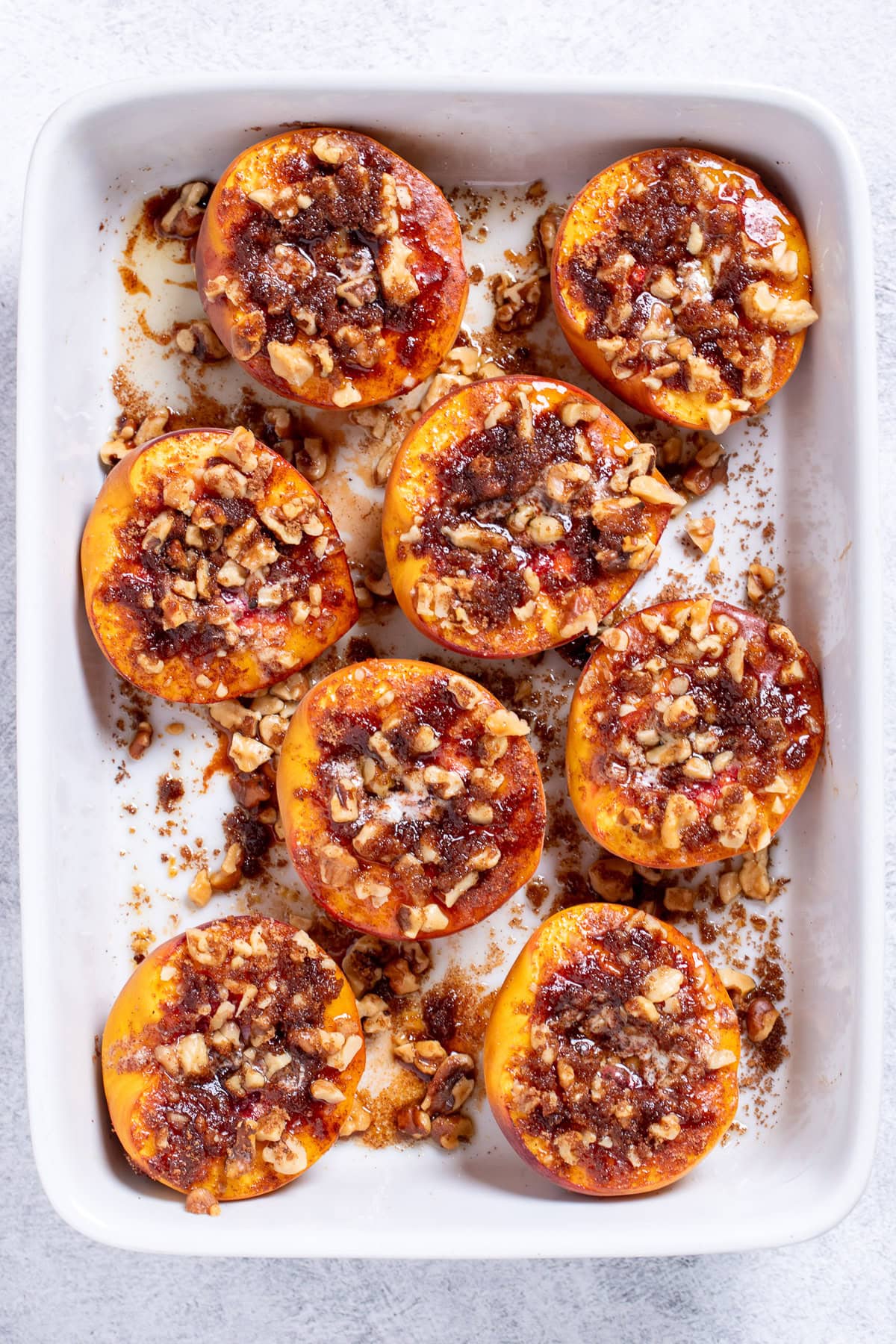 Baked peaches topped with brown sugar and pecans in a baking dish.