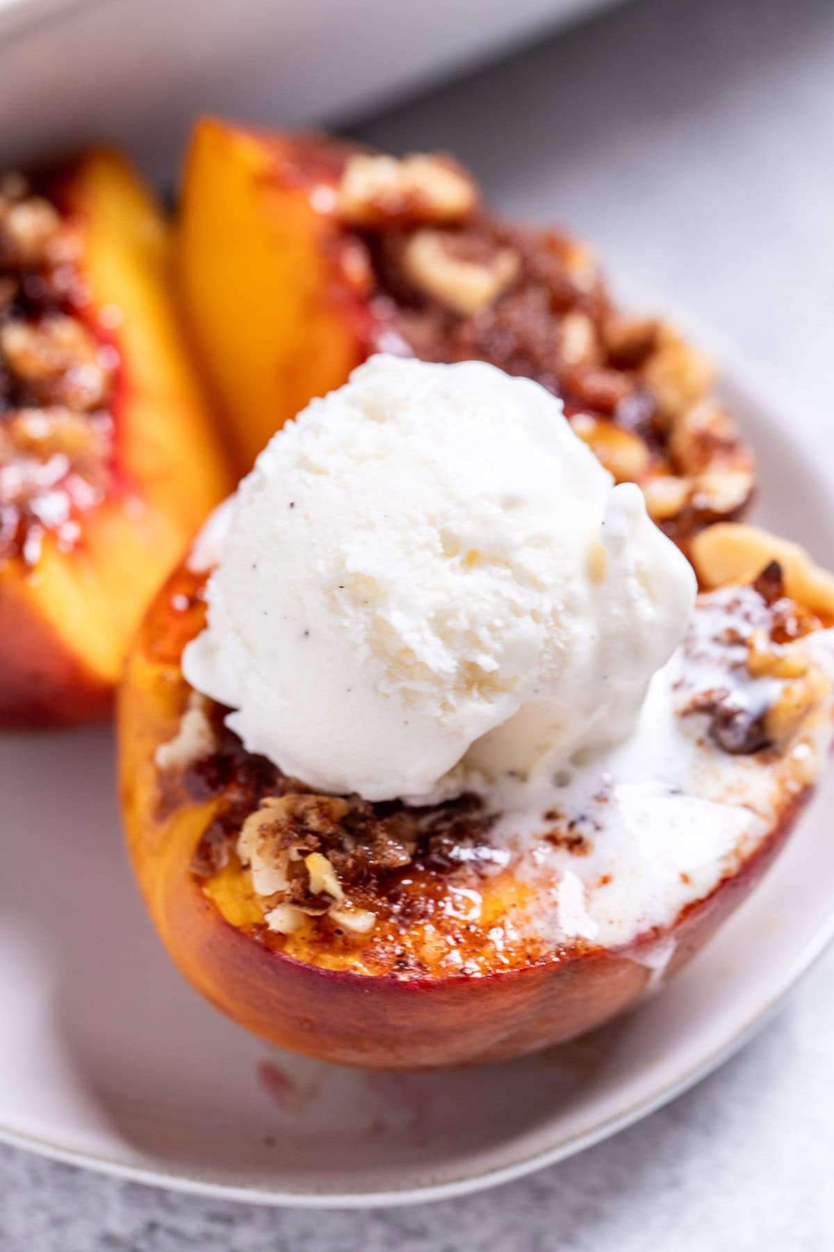 Baked peaches on a plate topped with brown sugar, pecans, and vanilla ice cream.