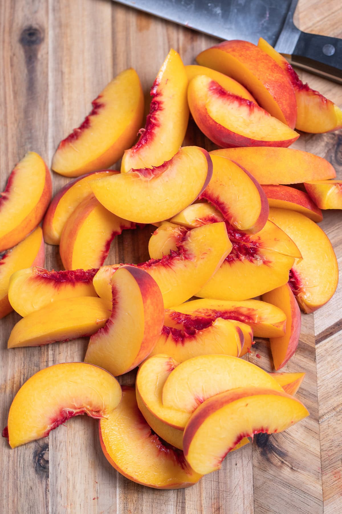 Peach slices sitting in a pile on a cutting board next to a knife.