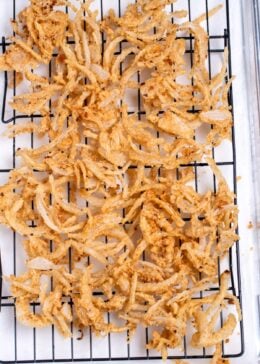 A sheet pan lined with paper towels and a baking rack, with crispy fried onions cooling after being fried.